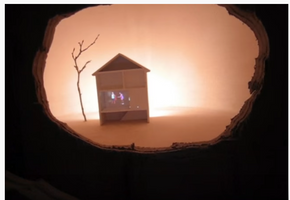 Liksom Duchamps ”Étant donnés” - ett hus med människor i videoprojektion, synligt geom hålet i väggen, murbruksbitar ligger i en hög på golvet...